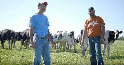 Two men standing in a field with dairy cows behind them.