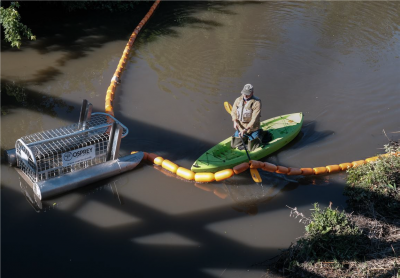 a man in a kayak adjusts floating boom using an oar