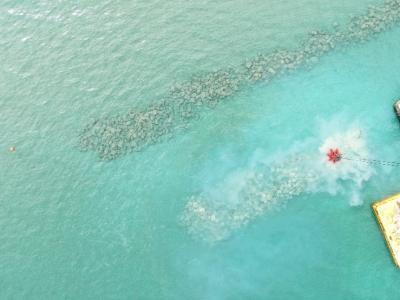 aerial view of a barge dropping stones into shallow water