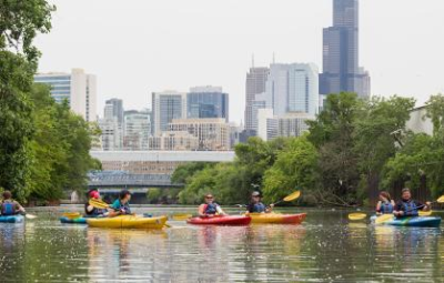 People kayaking on a river with a city skyline visible in the background.