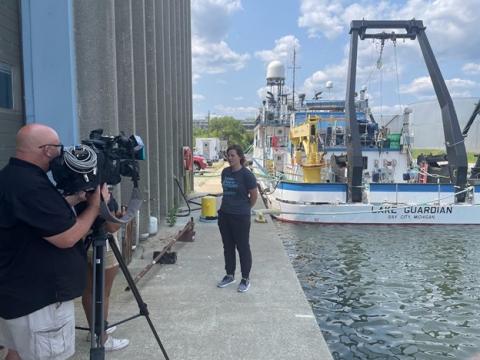 Megan O’Brien answers questions for a TV interview about the 2023 Summer Survey with the R/V Lake Guardian in the background.""