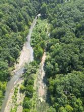 Aerial view of a stream channel in a forest with adjacent canal areas filled with flood water.  