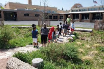 Photo of a group of school kids learning in the newly built bioswale in a school yard, in Milwaukee, Wisconsin.